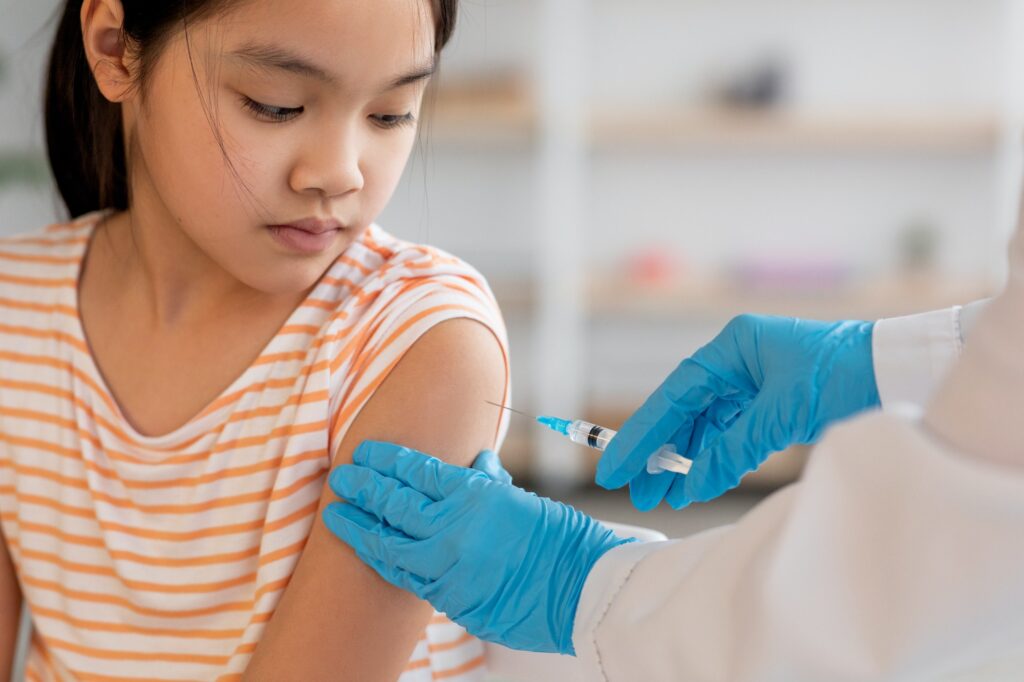 Unrecognizable nurse making vaccination for asian girl